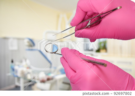 Dentist's hands with tweezers and mouth mirror. 92697802