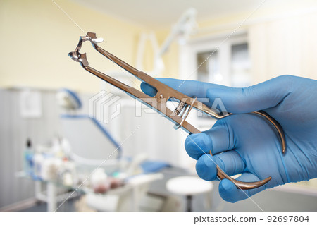 Dentist's hand in glove with rubber dam clamp forceps and clamp. 92697804