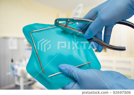 Dentist's hands in gloves with dental punch and cofferdam scarf. Dentist's hands in gloves with dental punch and cofferdam scarf. 92697806