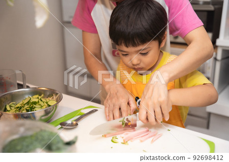 A 4-year-old boy learns how to cut ham with a child's knife from his mother A 4-year-old boy learns how to cut ham with a child's knife from his mother 92698412