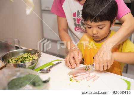 A 4-year-old boy learns how to cut ham with a child's knife from his mother A 4-year-old boy learns how to cut ham with a child's knife from his mother 92698415