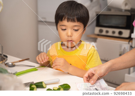 一個 4 歲的男孩試圖切黃瓜幫媽媽做飯 92698433