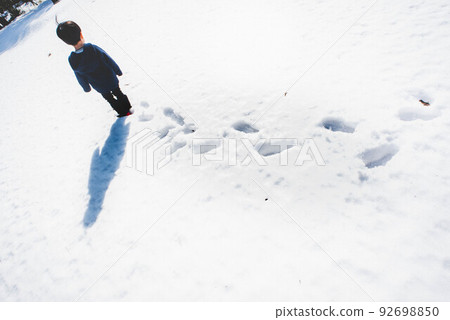 A child walking step by step on a snowy road where no one is walking 92698850