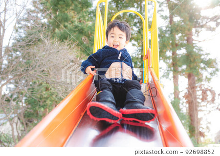 A child happily sliding down a slide 92698852