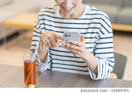 Close-up of a middle-aged woman drinking iced tea while looking at her smartphone in a cafe Close-up of a middle-aged woman drinking iced tea while looking at her smartphone in a cafe 92699765