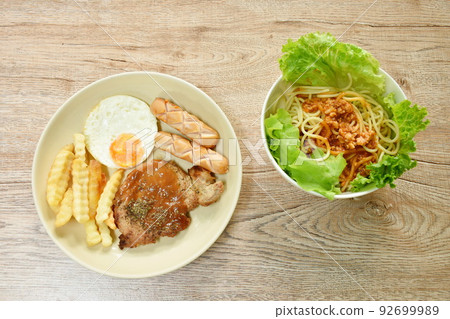 grilled pork steak dressing gravy sauce with french fries and fried egg couple sausage on plate and spaghetti dressing fried chop pork and slice tomato in ketchup sauce with vegetableon in bowl 92699989