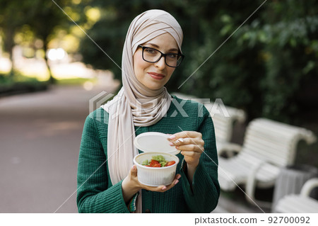 Cheerful muslim woman eating healthy lunch outdoor. 92700092
