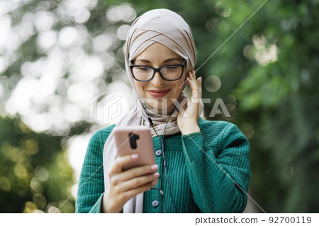 Young muslim woman listening to music while walking down a city park. Young muslim woman listening to music while walking down a city park. 92700119