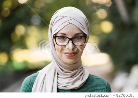 Portrait of young muslim woman wearing hijab head scarf in city park while looking at camera. 92700193