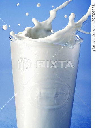 pouring milk in a glass isolated against blue background 92704358