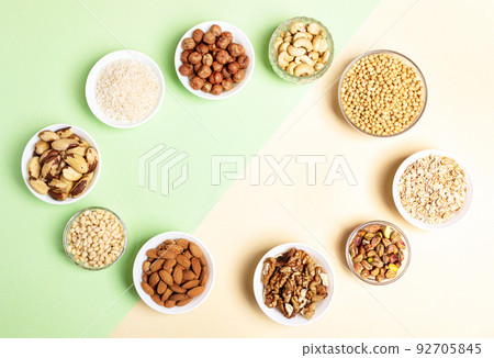 Oval frame of bowls with cereal grains and nuts on two-tone beige-green backdrop. Diet or nutrition concept. Superfoods. Vegan protein source. Healthy food. Top view. Horizontal shot. Copy space. Oval frame of bowls with cereal grains and nuts on two-tone beige-green backdrop. Diet or nutrition concept. Superfoods. Vegan protein source. Healthy food. Top view. Horizontal shot. Copy space. 92705845