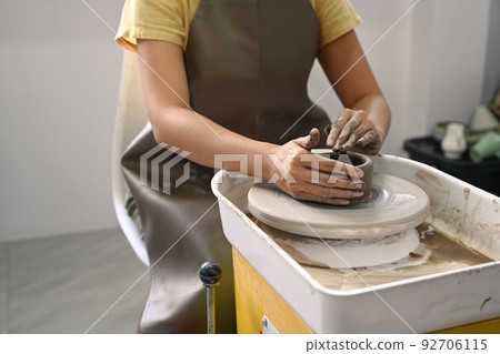 Cropped view of young woman wearing apron creating handmade ceramic bowl in pottery workshop 92706115