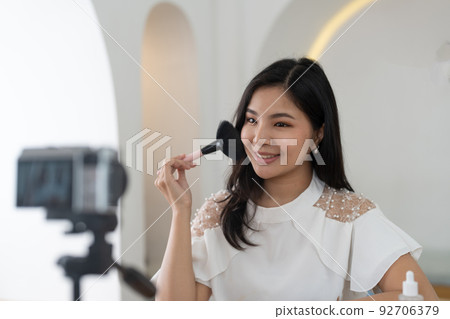 Famous blogger. Cheerful female vlogger is showing cosmetics products while recording video and giving advices for her beauty blog. 92706379