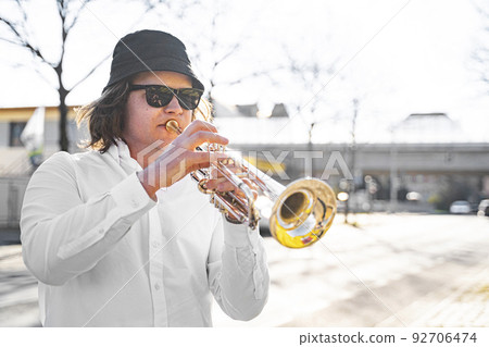 Young caucasian long-haired man in shirt and sunglasses playing trumpet outdoor Young caucasian long-haired man in shirt and sunglasses playing trumpet outdoor 92706474
