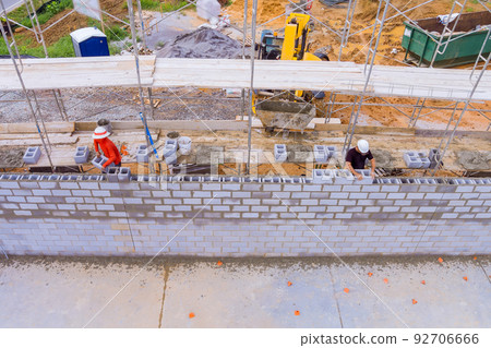 Construction site workers on scaffolding laying masonry cinder concrete blocks Construction site workers on scaffolding laying masonry cinder concrete blocks 92706666
