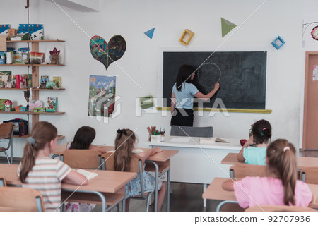 Elementary school. The female teacher helping the child student while writing the answer on the chalkboard. 92707936