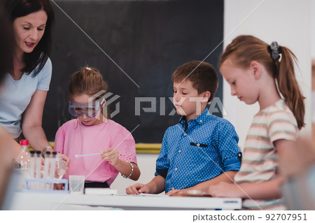 Elementary School Science Classroom: Enthusiastic Teacher Explains Chemistry to Diverse Group of Children, Little Boy Mixes Chemicals in Beakers. Children Learn with Interest 92707951