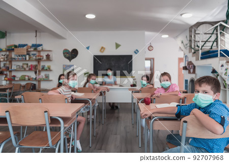 Multiracial group of kids wearing face masks working at class, writing and listening explanations of teacher in classroom 92707968