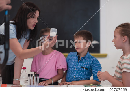 Elementary School Science Classroom: Enthusiastic Teacher Explains Chemistry to Diverse Group of Children, Little Boy Mixes Chemicals in Beakers. Children Learn with Interest Elementary School Science Classroom: Enthusiastic Teacher Explains Chemistry to Diverse Group of Children, Little Boy Mixes Chemicals in Beakers. Children Learn with Interest 92707969