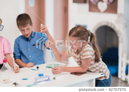 Elementary School Science Classroom: Enthusiastic Teacher Explains Chemistry to Diverse Group of Children, Little Boy Mixes Chemicals in Beakers. Children Learn with Interest Elementary School Science Classroom: Enthusiastic Teacher Explains Chemistry to Diverse Group of Children, Little Boy Mixes Chemicals in Beakers. Children Learn with Interest 92707970