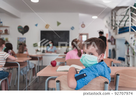 Multiracial group of kids wearing face masks working at class, writing and listening explanations of teacher in classroom Multiracial group of kids wearing face masks working at class, writing and listening explanations of teacher in classroom 92707974
