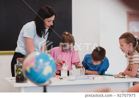 Elementary School Science Classroom: Enthusiastic Teacher Explains Chemistry to Diverse Group of Children, Little Boy Mixes Chemicals in Beakers. Children Learn with Interest Elementary School Science Classroom: Enthusiastic Teacher Explains Chemistry to Diverse Group of Children, Little Boy Mixes Chemicals in Beakers. Children Learn with Interest 92707975