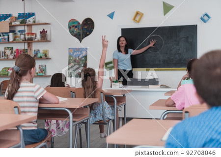 Elementary school. The female teacher helping the child student while writing the answer on the chalkboard. 92708046