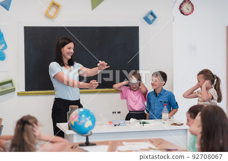 Elementary School Science Classroom: Enthusiastic Teacher Explains Chemistry to Diverse Group of Children, Little Boy Mixes Chemicals in Beakers. Children Learn with Interest Elementary School Science Classroom: Enthusiastic Teacher Explains Chemistry to Diverse Group of Children, Little Boy Mixes Chemicals in Beakers. Children Learn with Interest 92708067