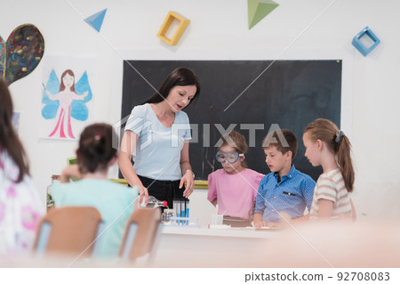 Elementary School Science Classroom: Enthusiastic Teacher Explains Chemistry to Diverse Group of Children, Little Boy Mixes Chemicals in Beakers. Children Learn with Interest Elementary School Science Classroom: Enthusiastic Teacher Explains Chemistry to Diverse Group of Children, Little Boy Mixes Chemicals in Beakers. Children Learn with Interest 92708083