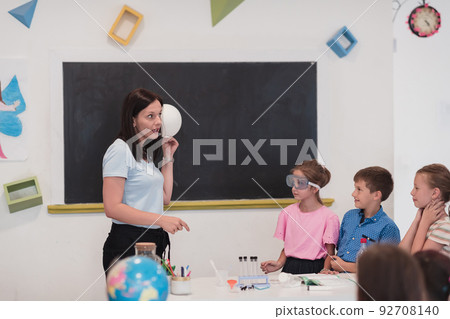 Elementary School Science Classroom: Enthusiastic Teacher Explains Chemistry to Diverse Group of Children, Little Boy Mixes Chemicals in Beakers. Children Learn with Interest 92708140