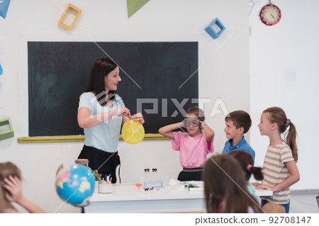 Elementary School Science Classroom: Enthusiastic Teacher Explains Chemistry to Diverse Group of Children, Little Boy Mixes Chemicals in Beakers. Children Learn with Interest Elementary School Science Classroom: Enthusiastic Teacher Explains Chemistry to Diverse Group of Children, Little Boy Mixes Chemicals in Beakers. Children Learn with Interest 92708147