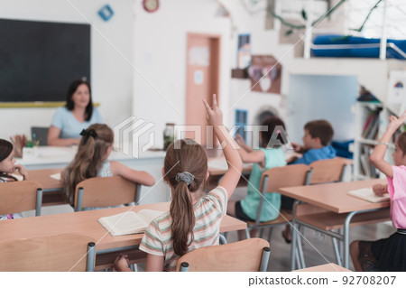 A teacher reads a book to elementary school students who listen carefully while sitting in a modern classroom 92708207