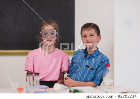 Elementary School Science Classroom: Enthusiastic Teacher Explains Chemistry to Diverse Group of Children, Little Boy Mixes Chemicals in Beakers. Children Learn with Interest 92708234