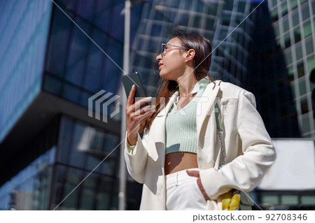 Attractive young woman in white suit calling friend stand near business centre Attractive young woman in white suit calling friend stand near business centre 92708346