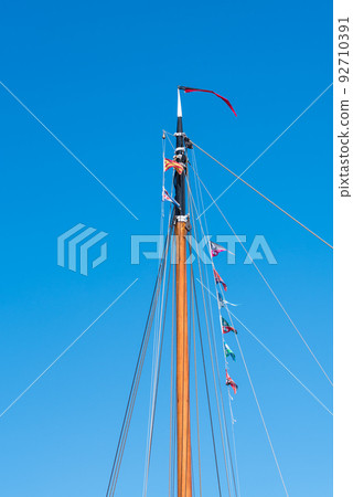 Den Helder, the Netherlands, May 2022. Close up of a mast with flag line against a blue sky. . Den Helder, the Netherlands, May 2022. Close up of a mast with flag line against a blue sky. . 92710391