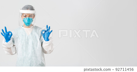 Covid-19, coronavirus disease, healthcare workers concept. Confident and serious asian female doctor, lab technician in personal protective equipment showing okay gesture in approval 92711456