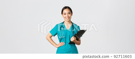 Healthcare workers, preventing virus, quarantine campaign concept. Smiling pleasant asian female physician, doctor during examination wearing scrubs and holding clipboard, white background Healthcare workers, preventing virus, quarantine campaign concept. Smiling pleasant asian female physician, doctor during examination wearing scrubs and holding clipboard, white background 92711603