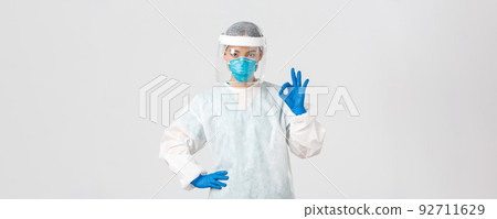 Covid-19, coronavirus disease, healthcare workers concept. Serious-looking professional female asian doctor in personal protective equipment, showing okay gesture, ensure safety of patient 92711629