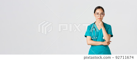 Covid-19, healthcare workers, pandemic concept. Serious-looking young female internet, asian nurse or physician in scrubs and glasses thinking, pondering or making choice, examine patient 92711674