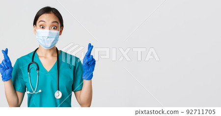 Covid-19, coronavirus disease, healthcare workers concept. Excited and hopeful asian female doctor, nurse in medical mask and rubber gloves cross fingers good luck, makign wish, white background Covid-19, coronavirus disease, healthcare workers concept. Excited and hopeful asian female doctor, nurse in medical mask and rubber gloves cross fingers good luck, makign wish, white background 92711705