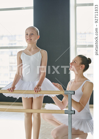 Young ballet teacher looking at youthful learner in white tutu at lesson 92711833