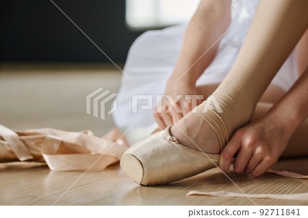 Close-up of hands of ballet dancer putting on pointe shoe before repetition Close-up of hands of ballet dancer putting on pointe shoe before repetition 92711841
