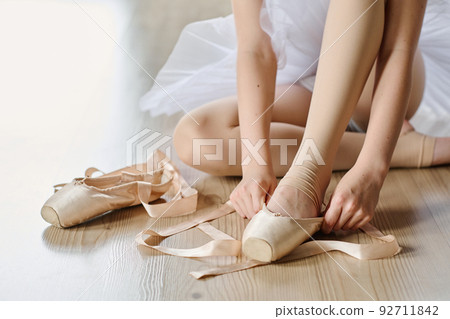 Hands of youthful ballet dancer tying silk beige ribbons on pointe shoe Hands of youthful ballet dancer tying silk beige ribbons on pointe shoe 92711842