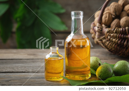 Bottles of essential nut oil, green and ripe walnuts. Basket of nuts on background. 92712050
