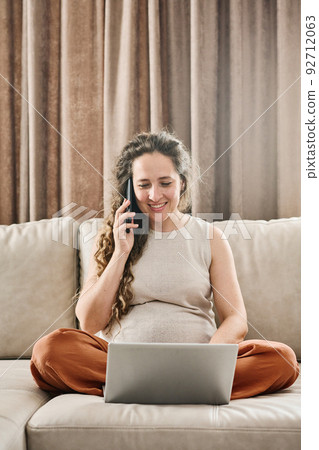 Young pregnant woman with long blond wavy hair ordering goods by phone 92712063