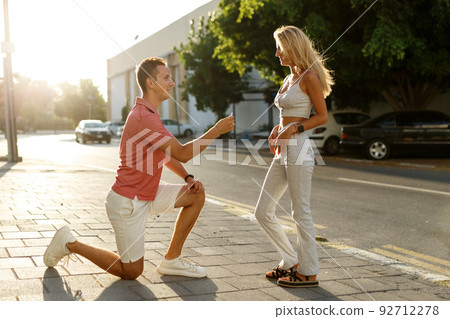 Young man with engagement ring making proposal to his beloved girlfriend outdoors.  92712278