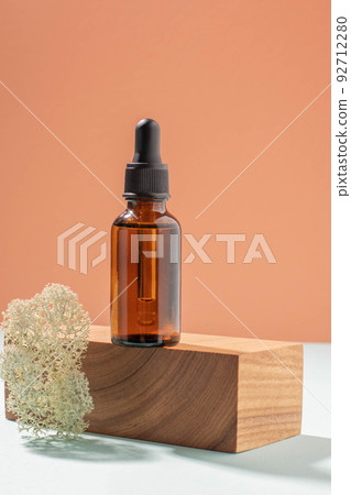 Bottle with pipette made of dark glass, cosmetic product woodenpedestal. Pastel coral background 92712280
