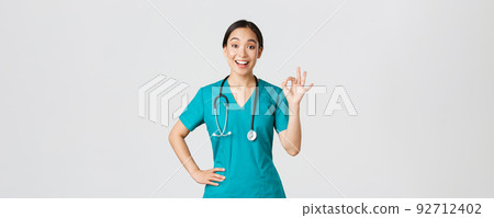 Covid-19, healthcare workers, pandemic concept. Surprised and happy asian female doctor, nurse in scrubs showing okay gesture and smiling amazed, praise nice work, agree with someone Covid-19, healthcare workers, pandemic concept. Surprised and happy asian female doctor, nurse in scrubs showing okay gesture and smiling amazed, praise nice work, agree with someone 92712402
