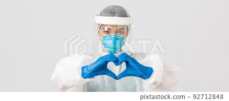Covid-19, coronavirus disease, healthcare workers concept. Close-up of confident and caring asian female doctor in personal protective equipment, showing heart gesture to patients 92712848