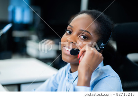 African young woman talking to a client on a headset. Female employee of the call center. 92713213